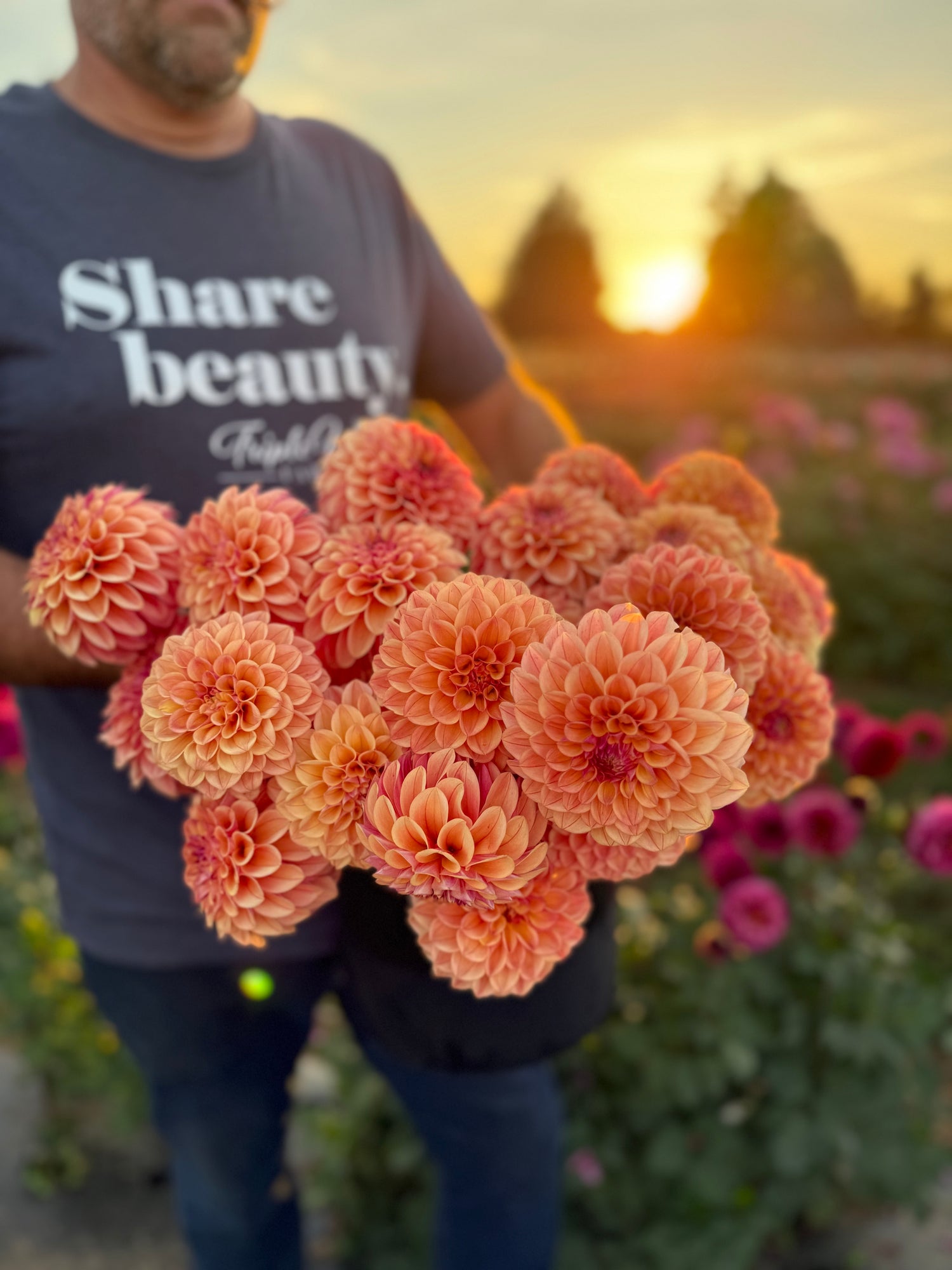 Person holding a large bouquet of peachy-orange  flowers with a sunset in the background.